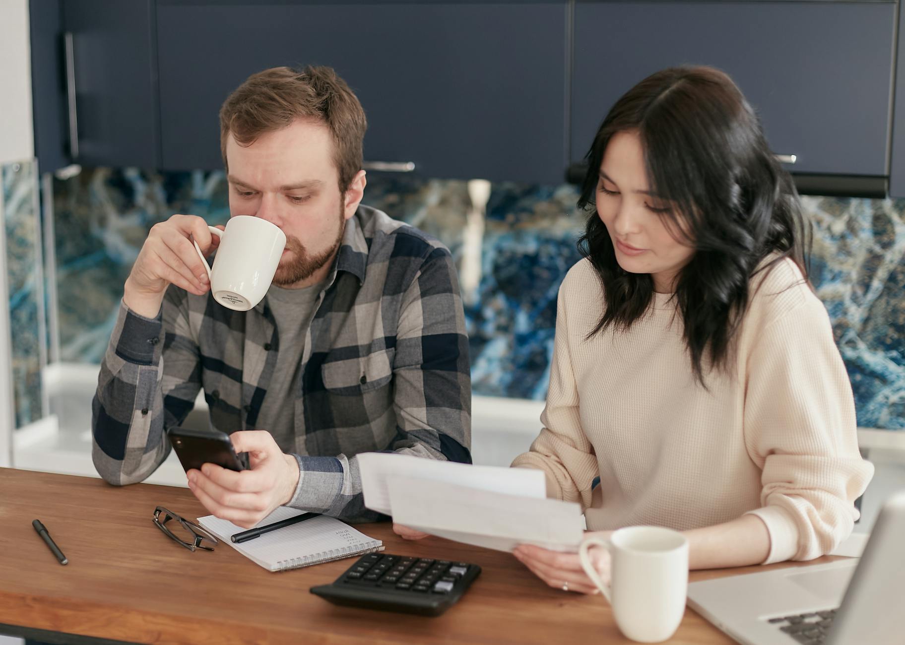 Para w kuchni licząca domowe koszty na kalkulatorze i smartfonie
