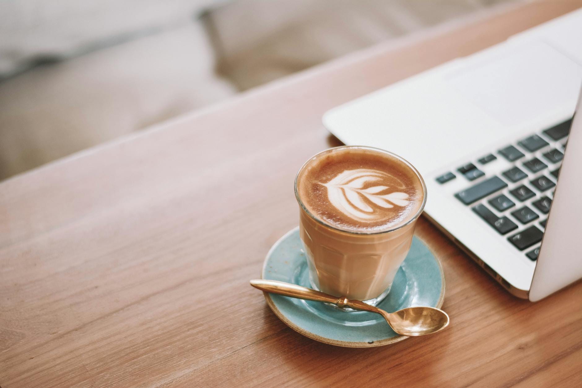 Szklanka latte z latte art obok laptopa na drewnianym biurku